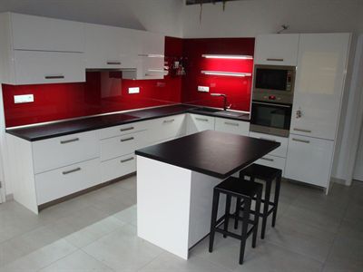 Kuchyňská linka do L v barvách bílé lesklé a černé se skleněným obkladem v červené barvě